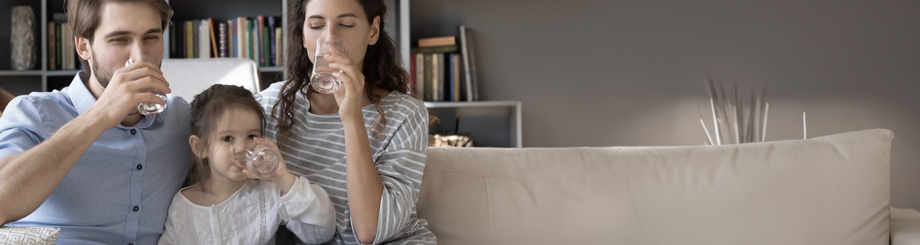 Eltern trinken mit Tochter auf dem Sofa ein Glas Wasser