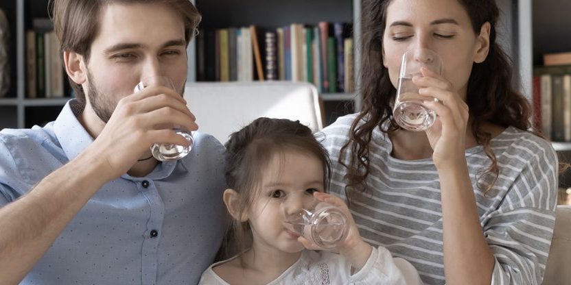 Eltern trinken mit Tochter auf dem Sofa ein Glas Wasser