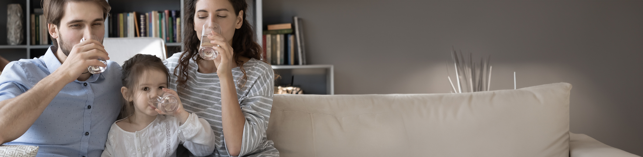 Eltern trinken mit Tochter auf Sofa ein Glas Wasser