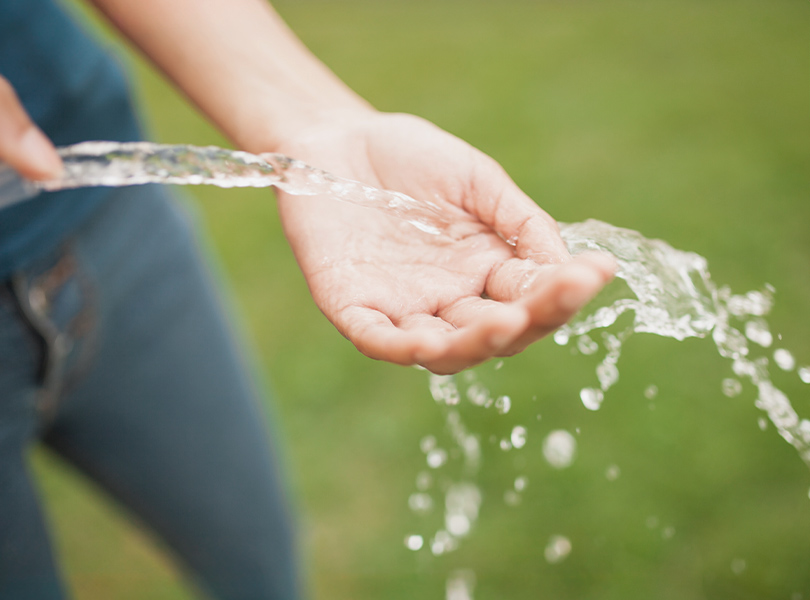 Person fängt Wasser aus Gartenschlauch mit Hand auf